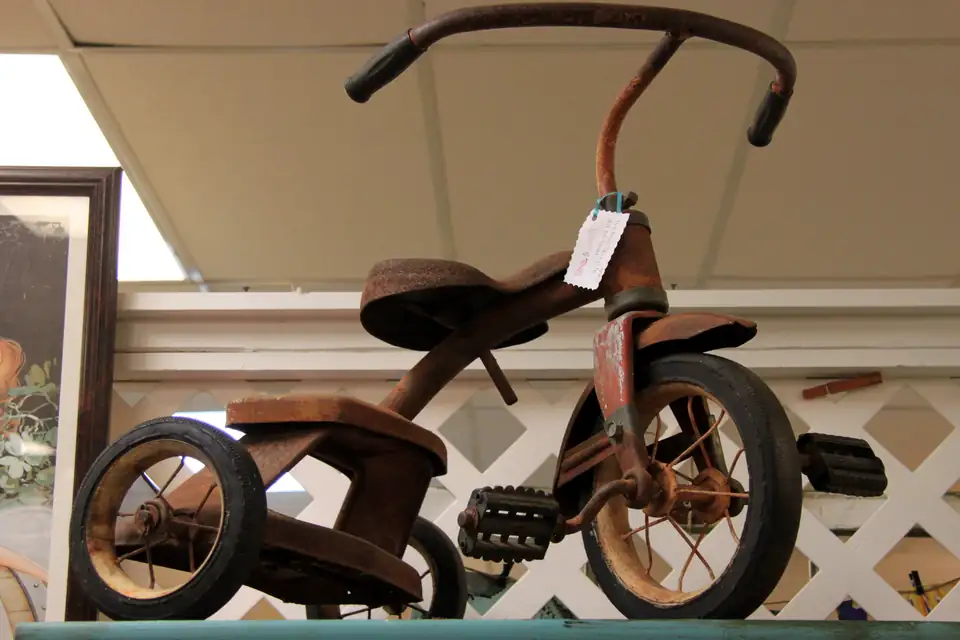 A rusty vintage tricycle with a price tag for sale in an antiques booth.