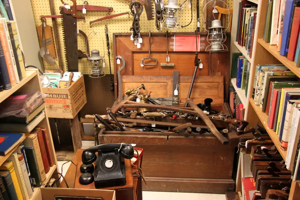 An antiques booth packed with an old carpenter's tool chest, lanterns, a rotary phone and shelves of books.