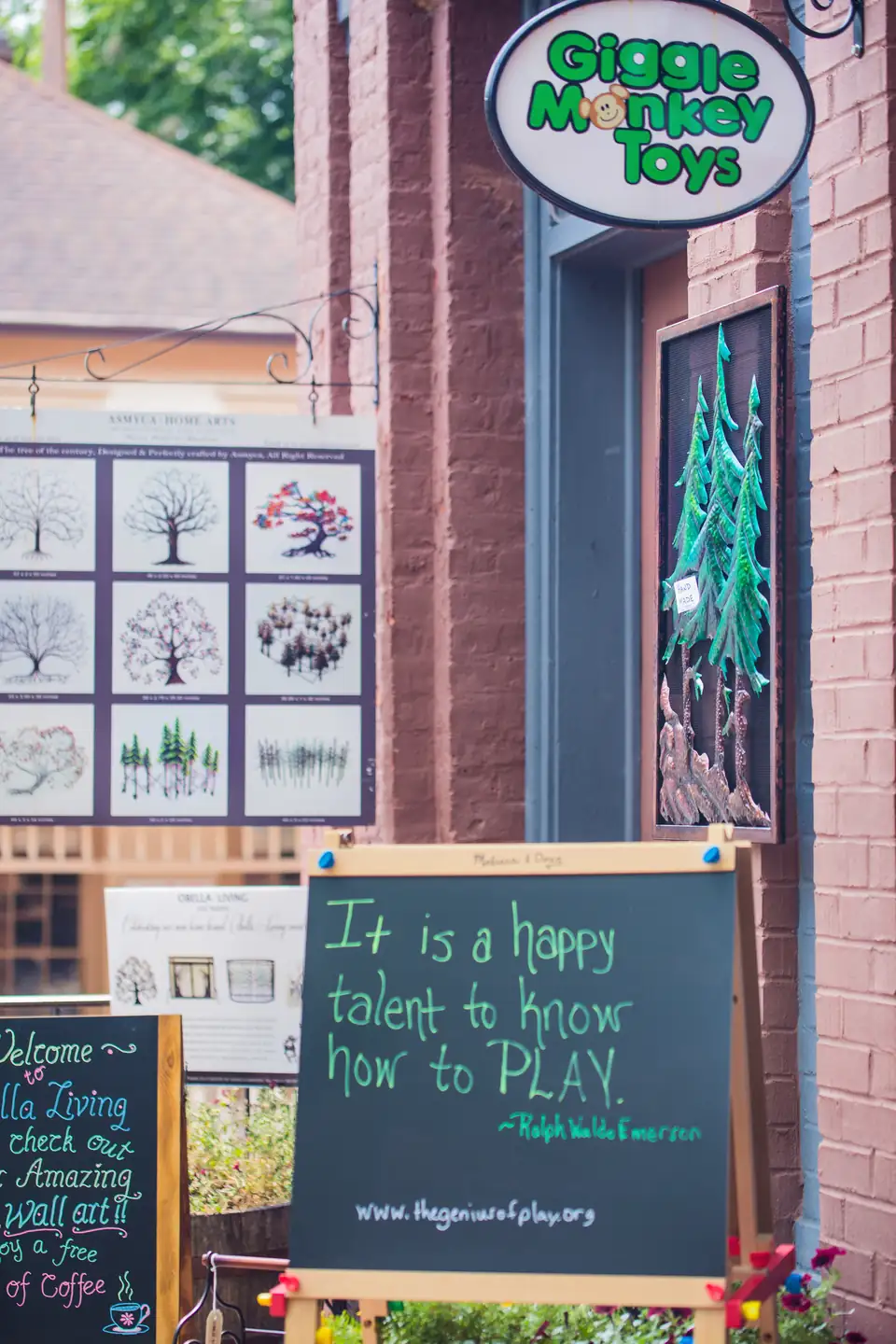 The hanging sign of Giggle Monkey Toys above a brick shop entrance with a chalkboard about play.