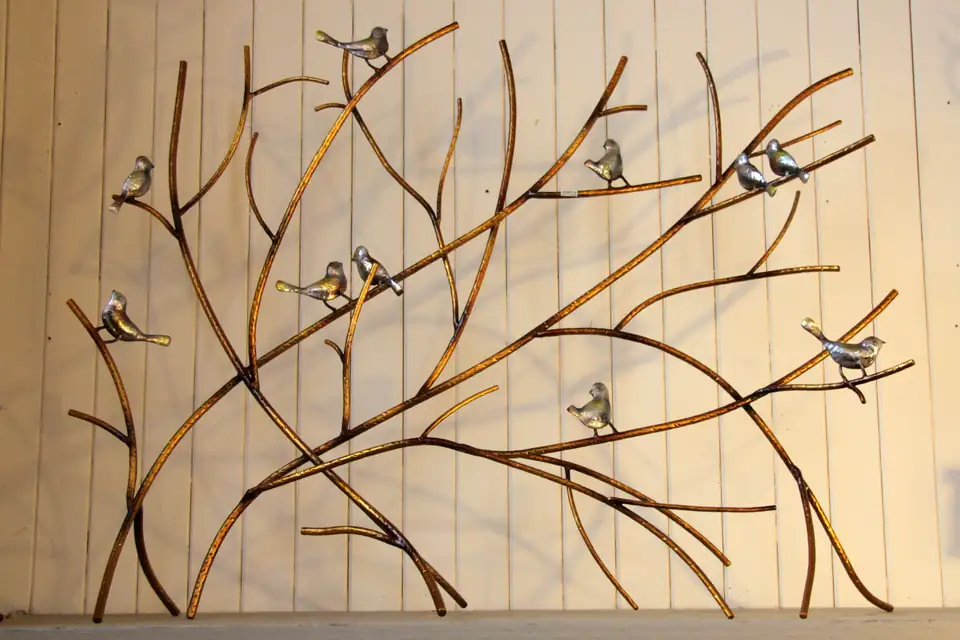 Metal wall art of golden branches with little silver birds, for sale on a shop wall.