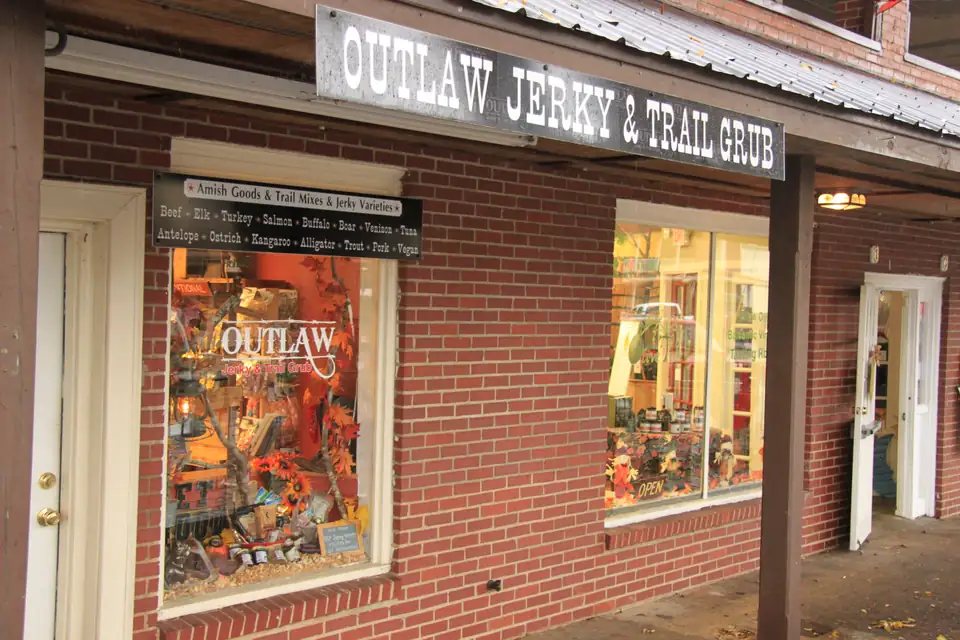 The brick front of Outlaw Jerky & Trail Grub with an autumn window display, next to an olive oil and vinegar tasting room window.