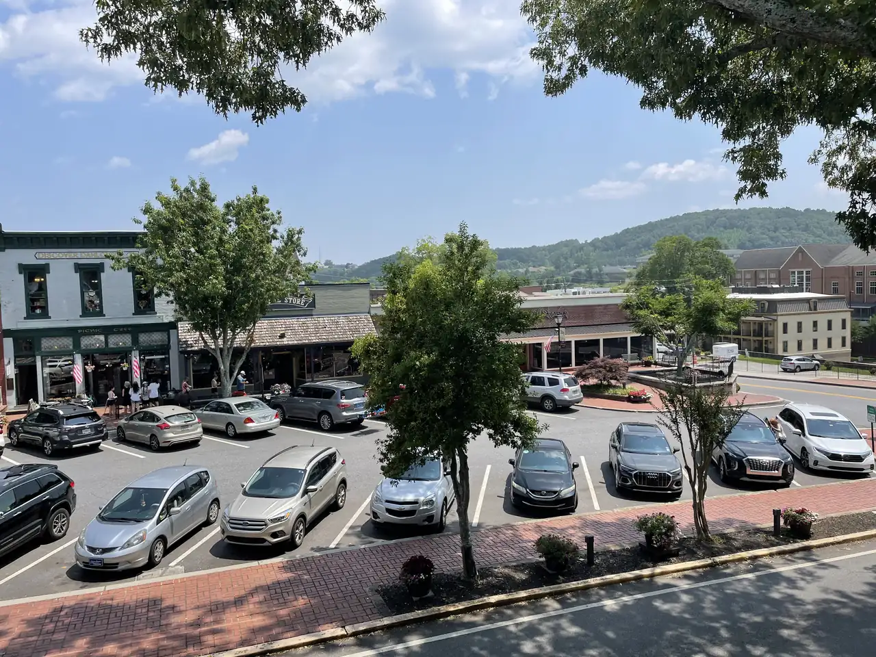 Looking down from the old courthouse across parked cars to the Picnic Cafe and general store fronts on the square, with wooded hills behind town.