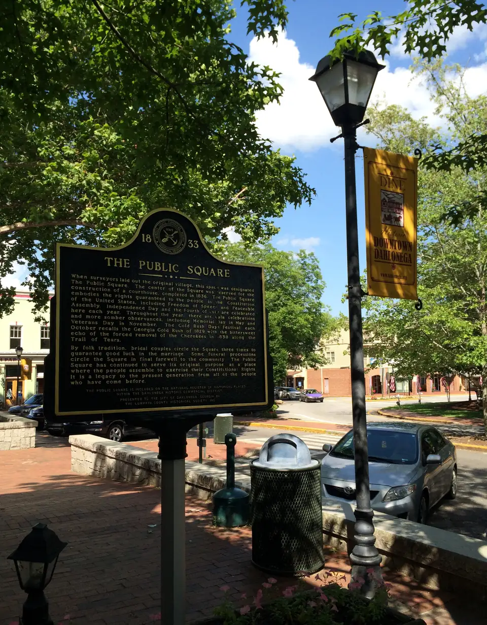 The historical marker for Dahlonega's Public Square on the brick plaza, with storefronts behind.