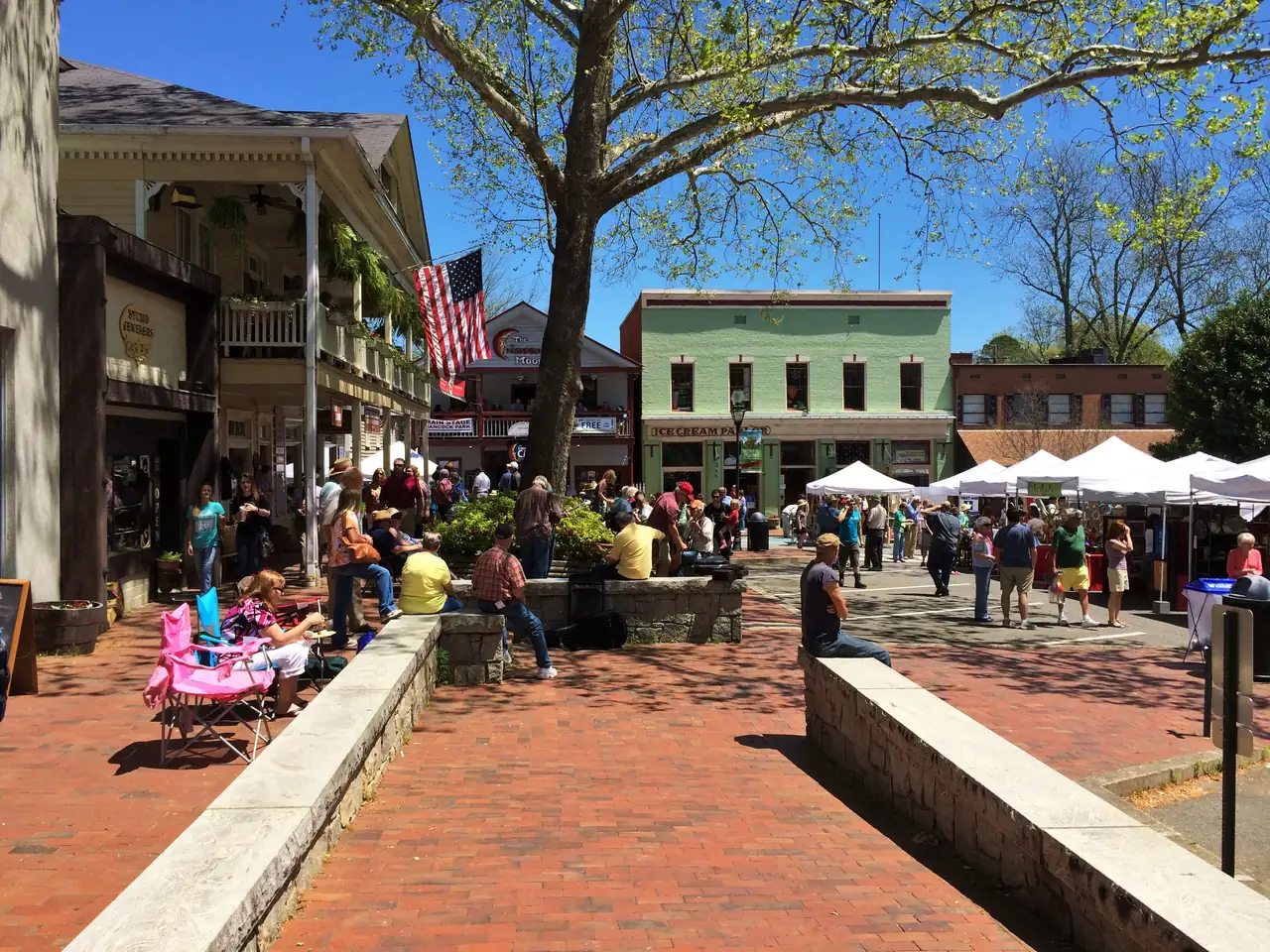 A crowded spring afternoon on Dahlonega's Public Square, with shoppers strolling past jewelry, music-venue and ice cream storefronts and white market tents in the street.